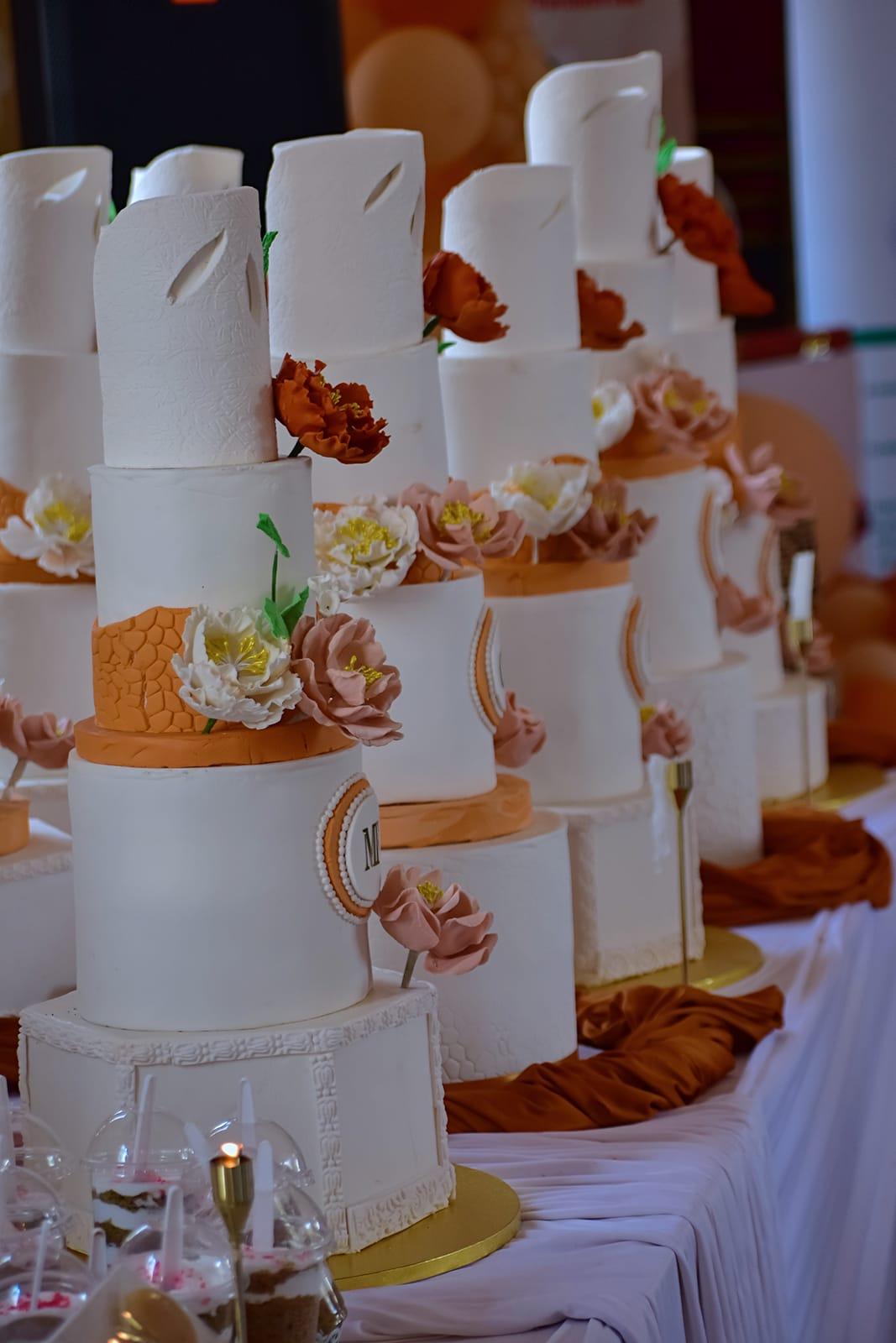 A row of elegant multi-tier wedding cakes with sugar flowers made by Modesh students